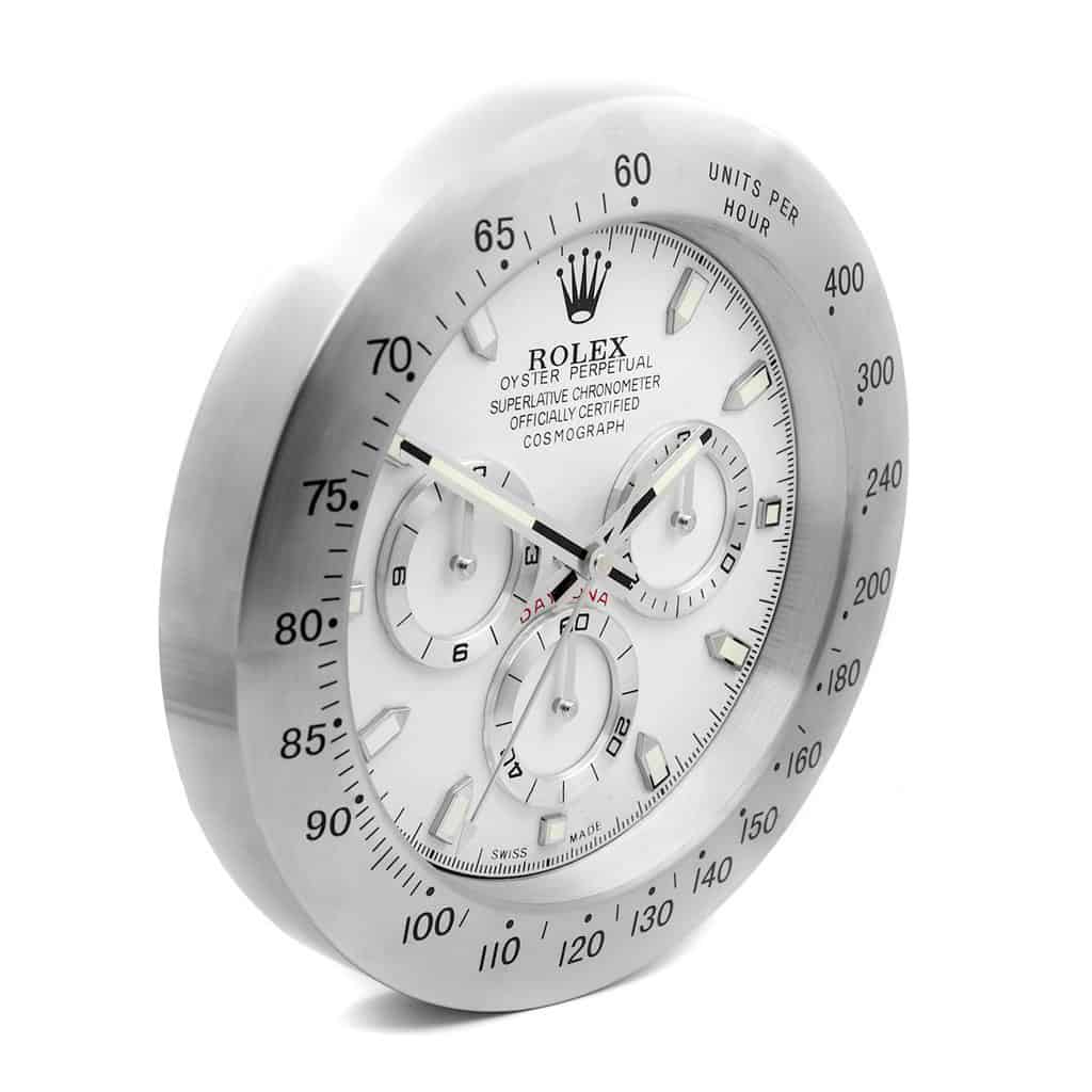Reloj de pared diseñado para parecerse a un Rolex Daytona con esfera plateada y detalles de cronógrafo.