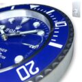 Close-up of a blue Rolex wall clock with white markings and silver hands, featuring a magnified date display and a ridged bezel.