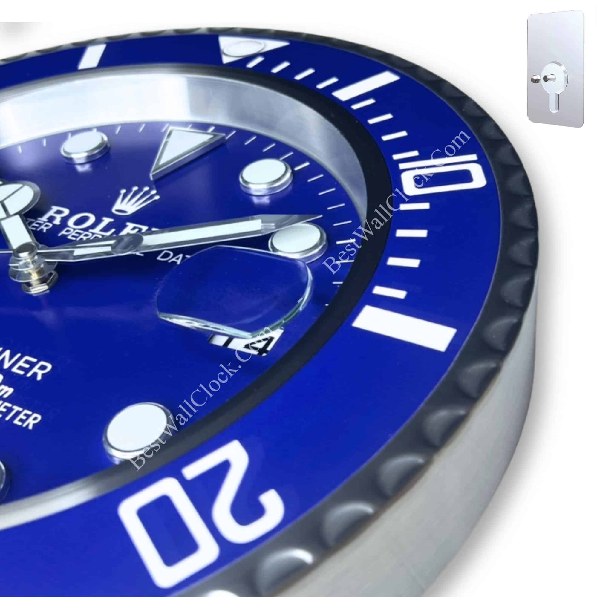 Close-up of a blue Rolex wall clock with white markings and silver hands, featuring a magnified date display and a ridged bezel.