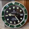 Close-up of a Rolex Submariner wall clock with a green and silver bezel, black dial, luminescent hour markers and hands, showing the date as 3 and the time as 9:23:45.