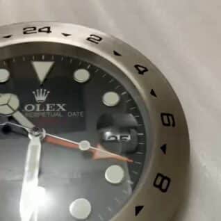 Close-up of a Rolex watch face showing hour markers, hands, and a date display magnified by a cyclops lens, with a stainless steel bezel featuring 24-hour markings.