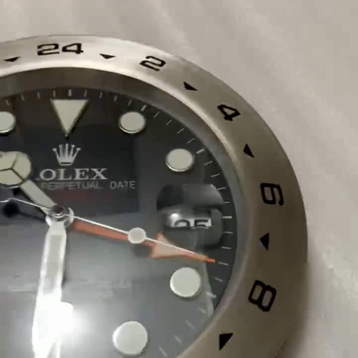 Close-up of a Rolex watch face showing hour markers, hands, and a date display magnified by a cyclops lens, with a stainless steel bezel featuring 24-hour markings.