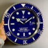 Hand holding a large wall clock designed to look like a blue Rolex Submariner watch face with white markers and hands, including a date window showing the number 30.
