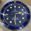 Close-up of a blue and gold Rolex Submariner clock face with luminous hour markers and hands, showing the time as 6:15 and a date window displaying the number 15