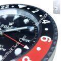 Close-up of a black and red rolex wall clock with white hour markers and hands, featuring a date magnifier and a silver bezel with a ridged edge