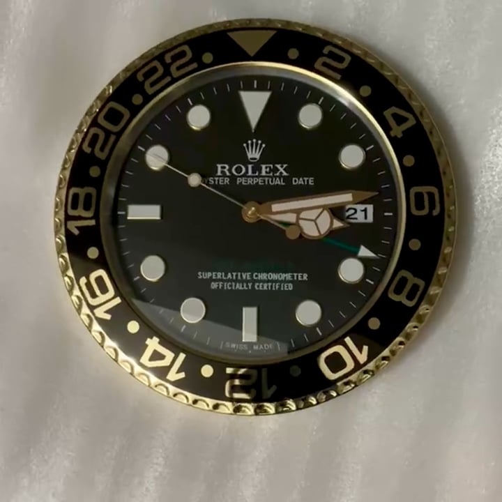 Close-up of a Rolex watch face with black dial, gold and black bezel marked with 24-hour numerals, and white hour markers, showing the date as 21 and text indicating it is a Superlative Chronometer Officially Certified.