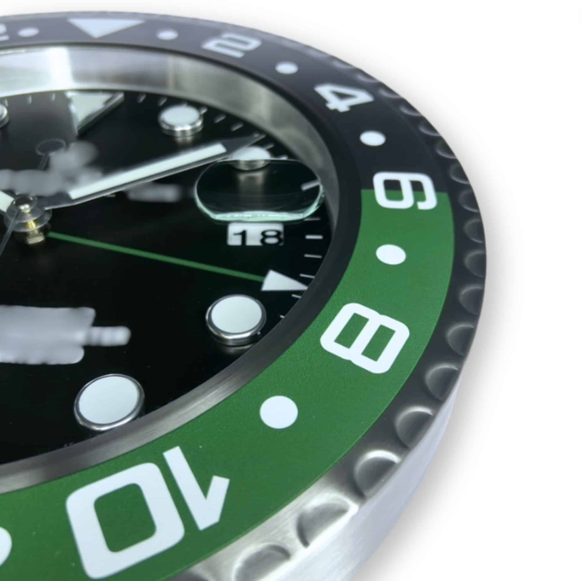 Close-up of a watch face showing the date as 18, with a green and black rotating bezel marked with numbers from 2 to 10, and luminous hour markers on a black dial.