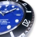 Close-up of a blue Rolex Submariner watch face showing the date as 22, with silver hour markers, white minute markers, and a black rotating bezel with white numbering and markers.
