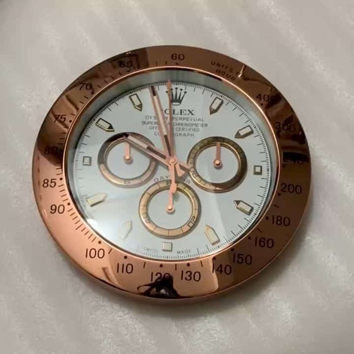 Close-up of a Rolex watch face with a rose gold bezel featuring detailed markings and subdials, on a light textured surface.