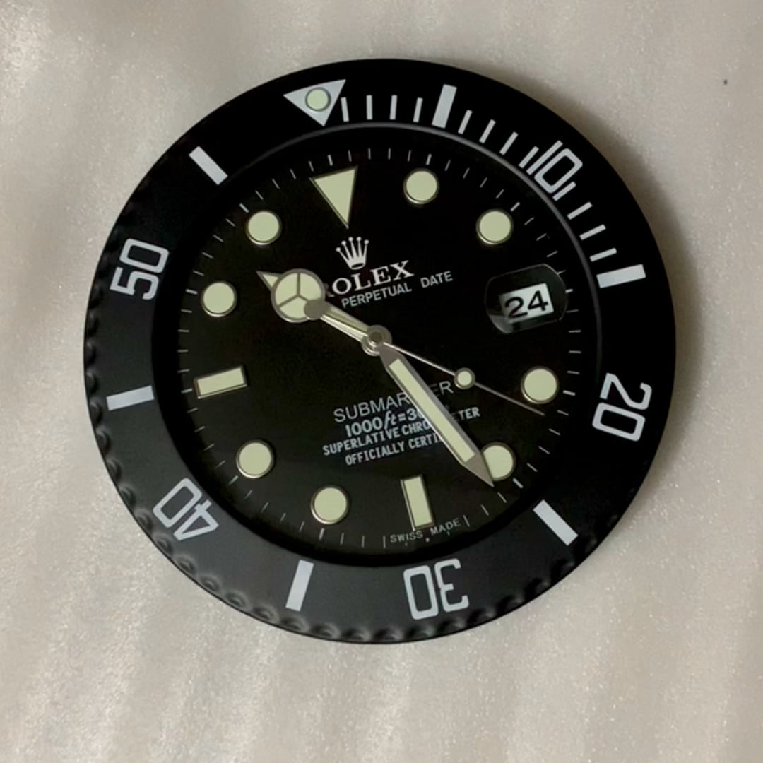 Close-up of a black Rolex Submariner watch face with luminous hour markers, showing the date as 24 and a bezel marked with minute indicators, placed on a light surface.