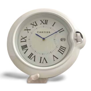 White-framed Cartier wall clock with Roman numerals, a white dial, blue hands, a date window, and a distinctive side crown.