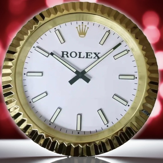 Close-up of a round gold Rolex clock with a white face, black hour and minute hands, and gold hour markers, set against a blurred red and pink background
