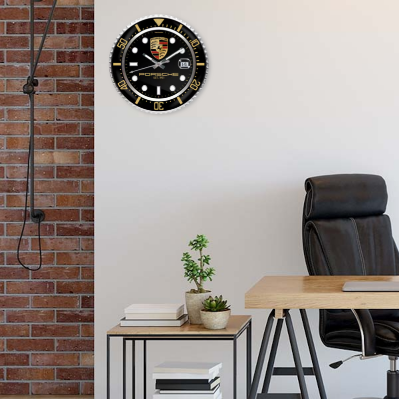 Modern home office with a black office chair, wooden desk, small plant, and a decorative wall clock against a brick wall featuring a Porsche Vintage Edition.