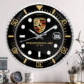 Wall-mounted clock with Porsche Vintage Edition branding and date display, in a room with decorative plants and a coffee cup.