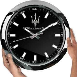 Hands holding a large round clock with a black face, white markers, Maserati logo and branding, and silver frame.