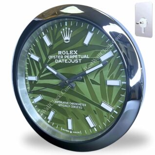 Round wall clock designed like a Rolex Oyster Perpetual Datejust watch face with green leaf pattern background, silver hour markers, and black glossy frame, mounted on a white wall with a keyhole hook beside it.