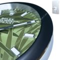 Close-up of a Rolex wall clock with a green geometric patterned dial, silver hour markers, and silver hands, showing part of the black frame and a separate mounting bracket on a white background.
