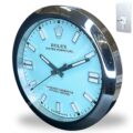 Wall clock designed like a Rolex Oyster Perpetual watch with a light blue face and silver markers, encased in a shiny metallic frame with a keyhole mounting plate beside it.