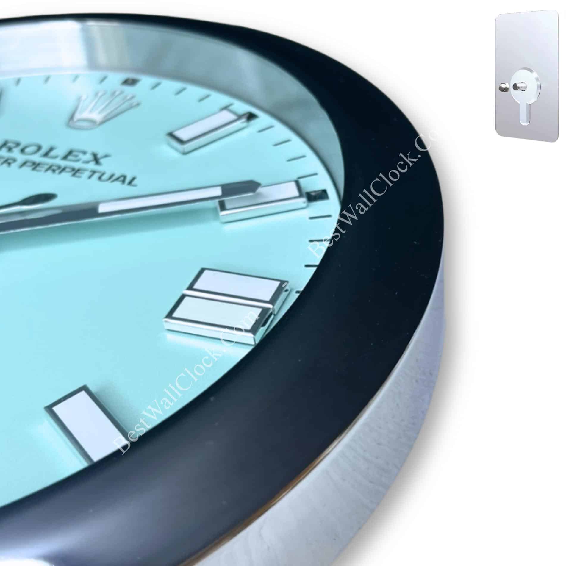 Close-up of a Rolex Air Perpetual wall clock with a blue face, silver hour markers, and black bezel, showing part of the clock's minute and hour hands.