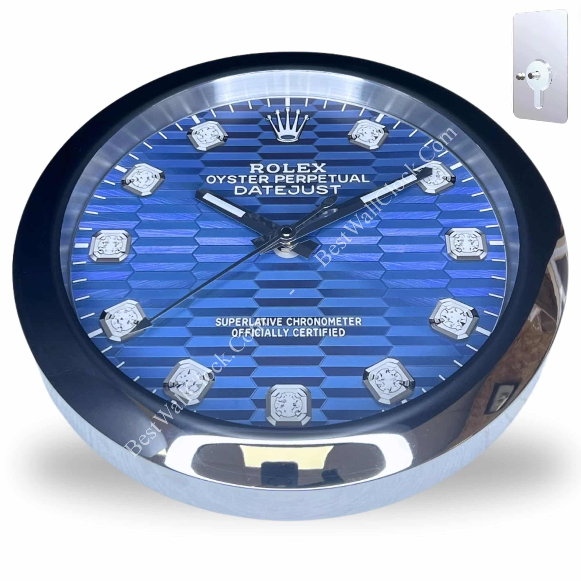 Round wall clock designed to resemble a Rolex Oyster Perpetual Datejust watch face with a blue patterned dial, silver markers, and silver hands, mounted on a silver base with a keyhole shown in the corner for wall mounting.