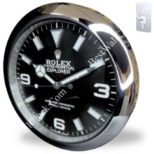 Rolex wall clock designed like a Rolex Oyster Perpetual Explorer watch with a black dial, white hour markers, silver frame, and a chrome wall mount in the background.