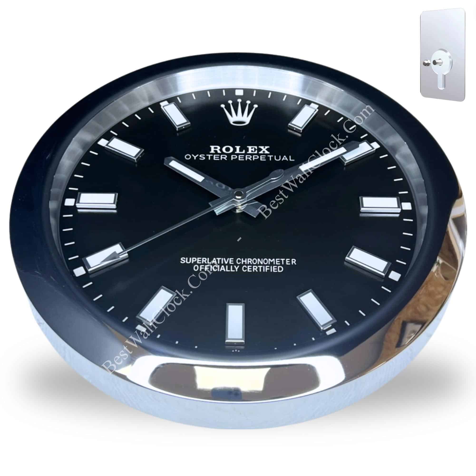 Rolex wall clock with a black dial and silver hour markers set in a round silver frame showing the time 10:10:38, mounted on a light background with a metal wall hook in the corner