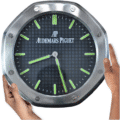A hands holding a Rolex wall clock designed in the style of an Audemars Piguet watch face with a metallic octagonal frame and green luminescent markers and hands on a black grid patterned background.
