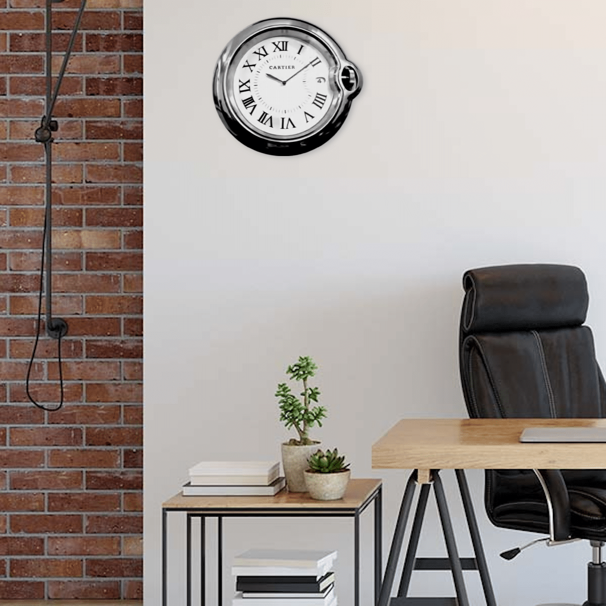 Rolex wall clock styled like a Cartier watch mounted on a white office wall above a wooden desk with a black leather chair, adjacent to a small table holding plants and books against a brick wall background.