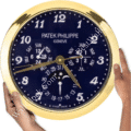 Close-up of a Patek Philippe wall clock with a dark blue face, gold frame, multiple dials showing days, months, and date, and two hands holding the clock, described as a rolex wall clock.