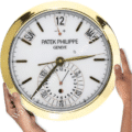rolex well clock showing time with gold rim, white face, date, day, and month indicators, held by two hands