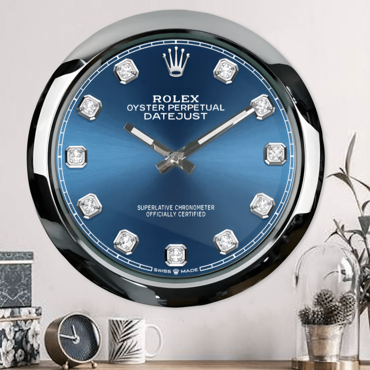 Rolex well clock featuring a large wall clock styled like a Rolex Oyster Perpetual Datejust with a blue dial and diamond markers in a modern interior setting with smaller clock, decorated mug, and plant.
