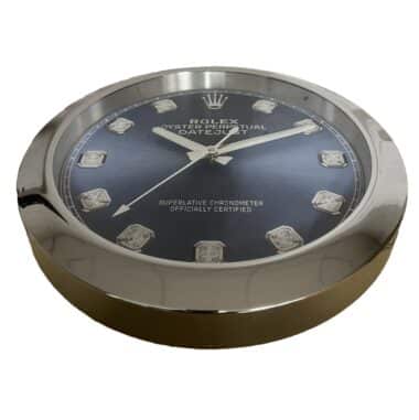 Rolex well clock showing a close-up of a silver-framed round dial with a blue face, silver hour markers, and silver hands displaying the time 10:12:40.