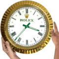 rolex well clock featuring a round gold frame, white face with black Roman numerals, green hour and minute hands, and two hands holding it on either side