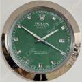 rolex well clock showing green face with silver hour markers and hands in a round chrome frame indicating time at 10:11:40 with date window at 3 o'clock