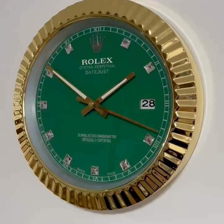 Close-up of a green Rolex Oyster Perpetual Datejust wall clock with a gold fluted bezel, diamond hour markers, and a date display showing the 28th, mounted on a white wall.