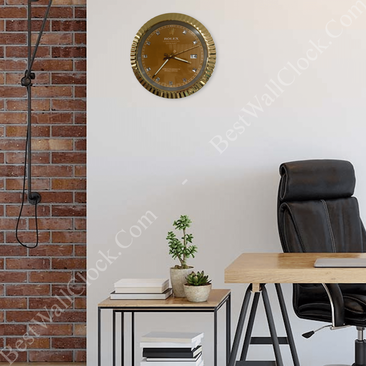Modern office space with a wooden desk, black ergonomic chair, small side table holding potted plants and books, and a gold-colored wall clock resembling a Rolex watch against a white wall with exposed brick on the left