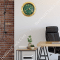 Modern office corner with a black leather chair, wooden desk, side table with small potted plants and books, and a green and gold Rolex-style wall clock with Roman numerals on a light wall next to an exposed brick section.