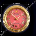 Round gold-colored wall clock with a red face, Roman numerals for hours, and three gold hands; includes date display showing '17', measures 14 inches (35 cm) in diameter and weighs 1.2 kg (2.6 lb), set against a black background.