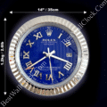 A round Rolex wall clock with a blue face, silver Roman numerals, and silver hands, measuring 14 inches (35 cm) in diameter, with a silver ridged frame weighing 1.2 kg (2.61 lb) on a dark background.