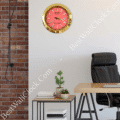 Modern office corner with a black leather chair, wooden desk, small table holding potted plants and books, and a gold-framed wall clock with a red face and white markers showing 4:40.