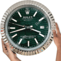 Hands holding a large round wall clock designed to resemble a Rolex Oyster Perpetual Datejust watch with a green patterned face, silver hour markers, and a date display showing the 16th, set against a white background.