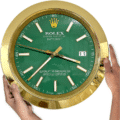 Hands holding a large gold-framed Rolex Oyster Perpetual Datejust wall clock with a green face displaying the time as 3:38:47 and the date as 11.