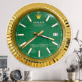 Wall clock designed to resemble a Rolex Datejust watch with a gold bezel, green face, white and gold hour markers, and date display showing 11, mounted on a white wall above a shelf with decorative items including a small clock, mug, and plants.