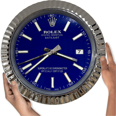 Hands holding a large Rolex Oyster Perpetual Datejust wall clock with a blue face and silver markings showing the time as 3:39:39 and the date as 7.