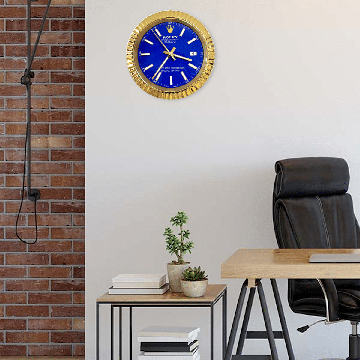 Modern office space with a black leather office chair, a wooden desk, a small side table with potted plants and stacked books, and a gold-framed blue Rolex wall clock on a white wall next to an exposed brick section.