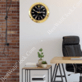 Modern office interior with a black and gold Rolex-themed wall clock above a small side table holding potted plants and books, a black leather office chair, and a wall with exposed red brick and a hanging black lamp.