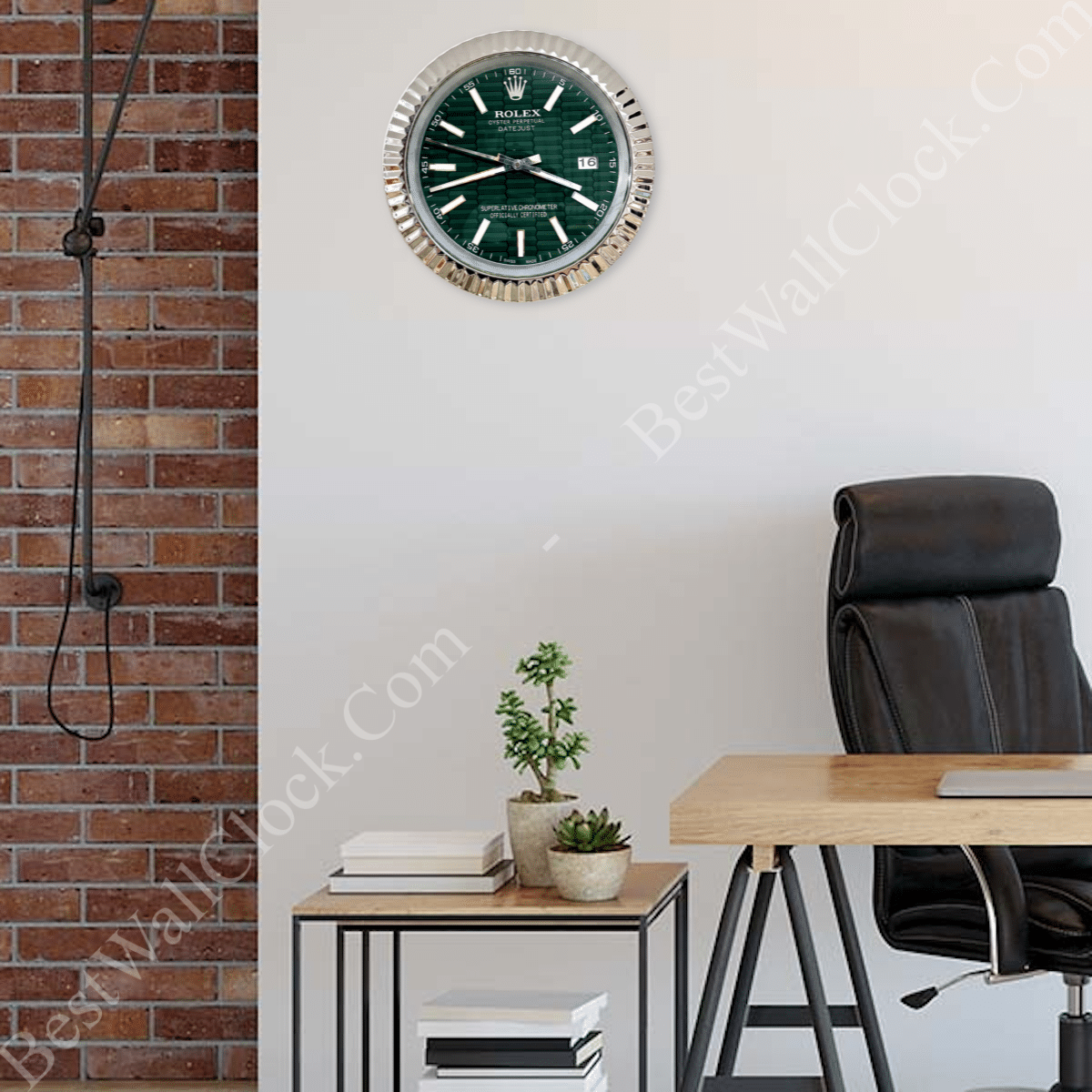 Modern office space with a black leather office chair, wooden desk, side table holding stacked books and two small potted plants, and a wall clock resembling a Rolex watch with a green face and silver bezel mounted on a white wall next to an exposed brick wall with a hanging cable.