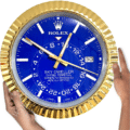 Hands holding a large Rolex Sky-Dweller wall clock with a blue dial and gold textured bezel showing the time at 12:51:18 with date 30