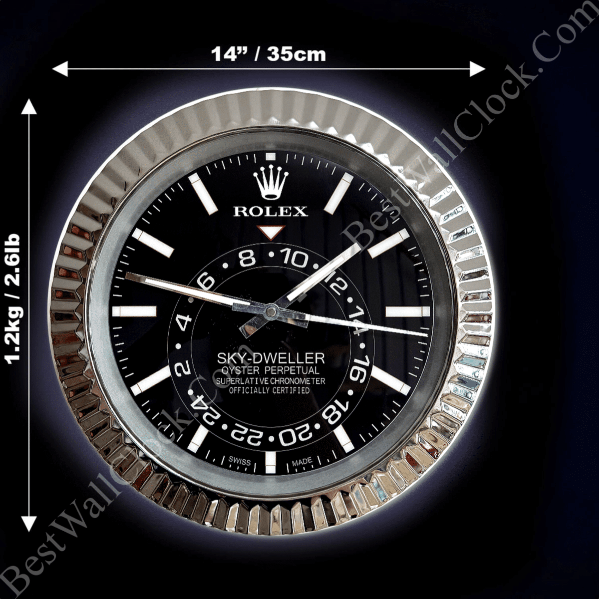 Close-up of a black Rolex Sky-Dweller wall clock with white hour markers and hands, showing the time as 10:10:15, surrounded by a silver fluted bezel against a black background with dimensions 14 inches (35 cm) in diameter and weight 1.2 kg (2.6 lb) indicated by white measurement arrows.
