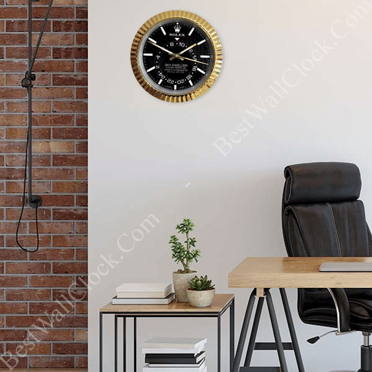 Modern office corner featuring a black and gold Rolex-themed wall clock above a small metal and wood side table with two potted plants and stacked books, next to a wooden desk with a black leather office chair, against a white wall and adjacent to an exposed red brick wall with a vintage industrial-style hanging lamp.
